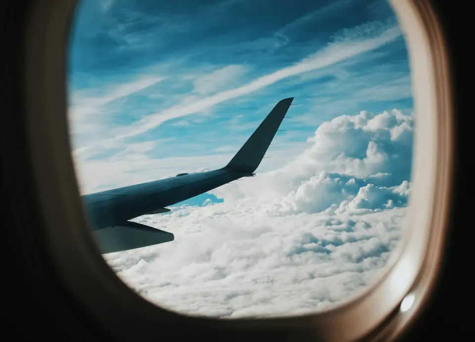 Asa de avião vista pela janela, acima das nuvens
